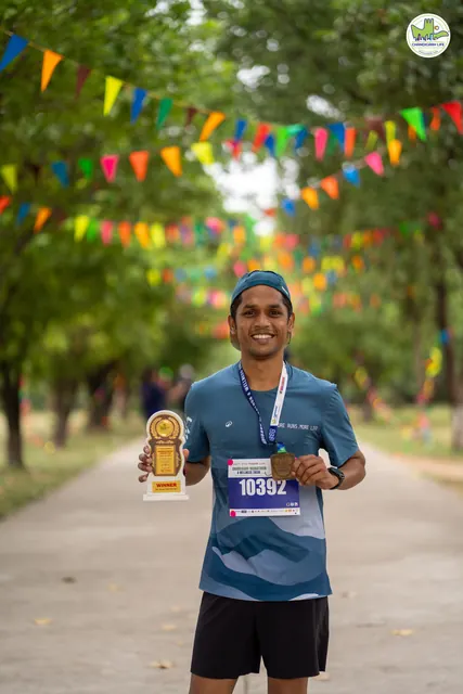 A runner holding a trophy under colourful bunting on a tree-lined path