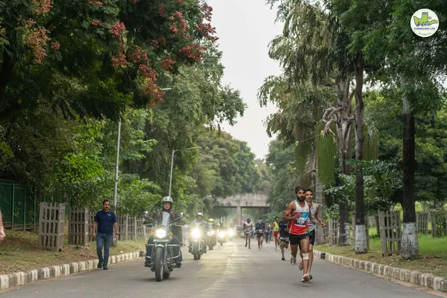Lead runners on a tree-lined avenue with a police motorcycle escort