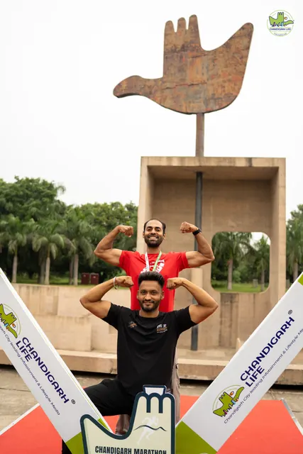 Two men flexing in front of the Open Hand Monument with event boards