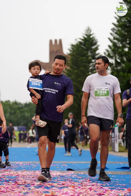 A man carrying a toddler as he finishes with another runner