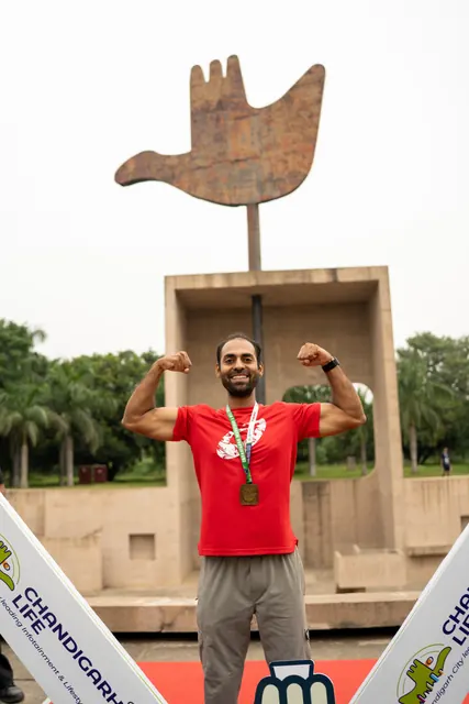 A man in red flexing in front of the Open Hand Monument